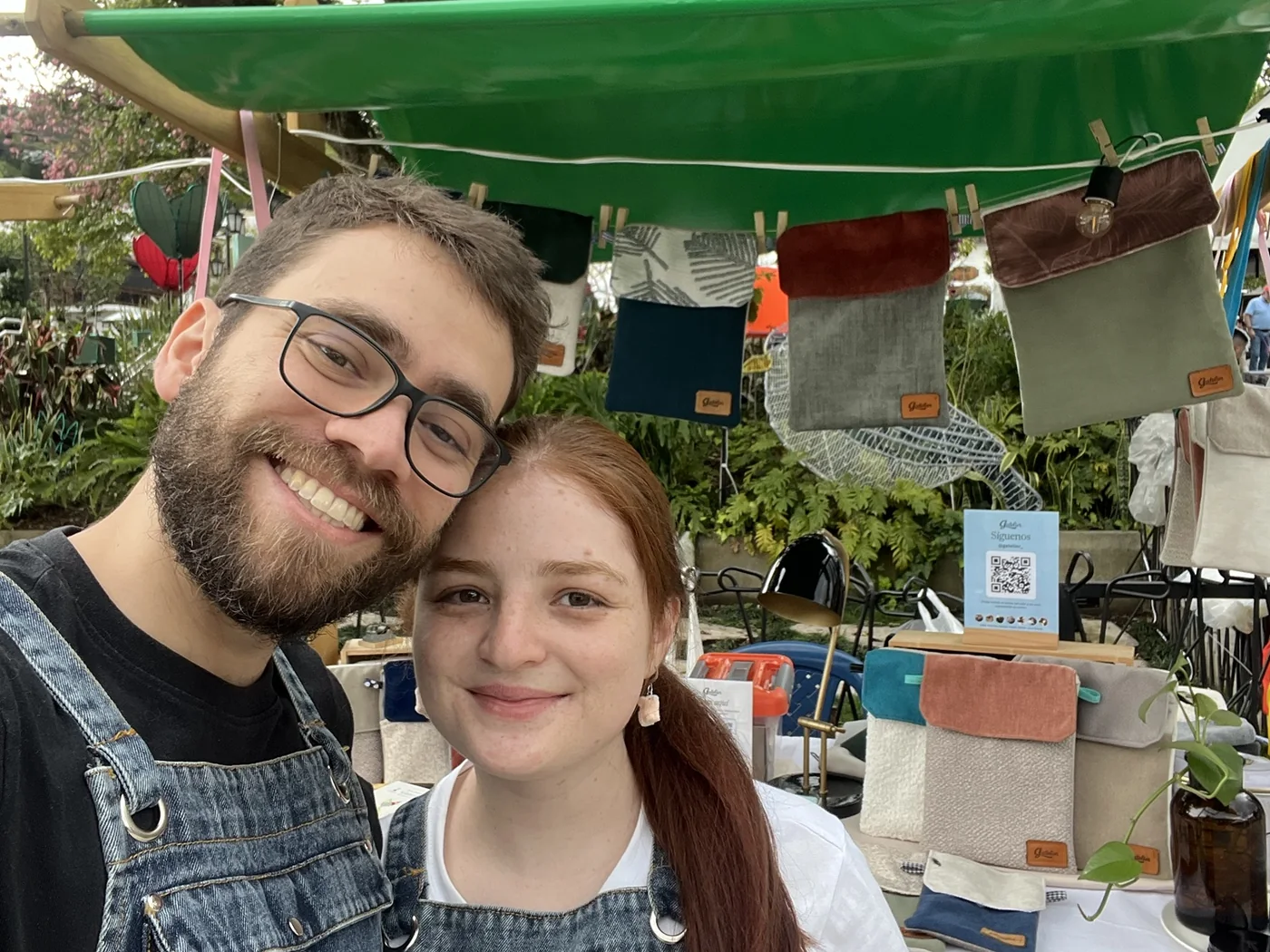 Juan Pablo y Salomé sonriendo en su puesto de Gatelier, con fundas colgadas detrás
